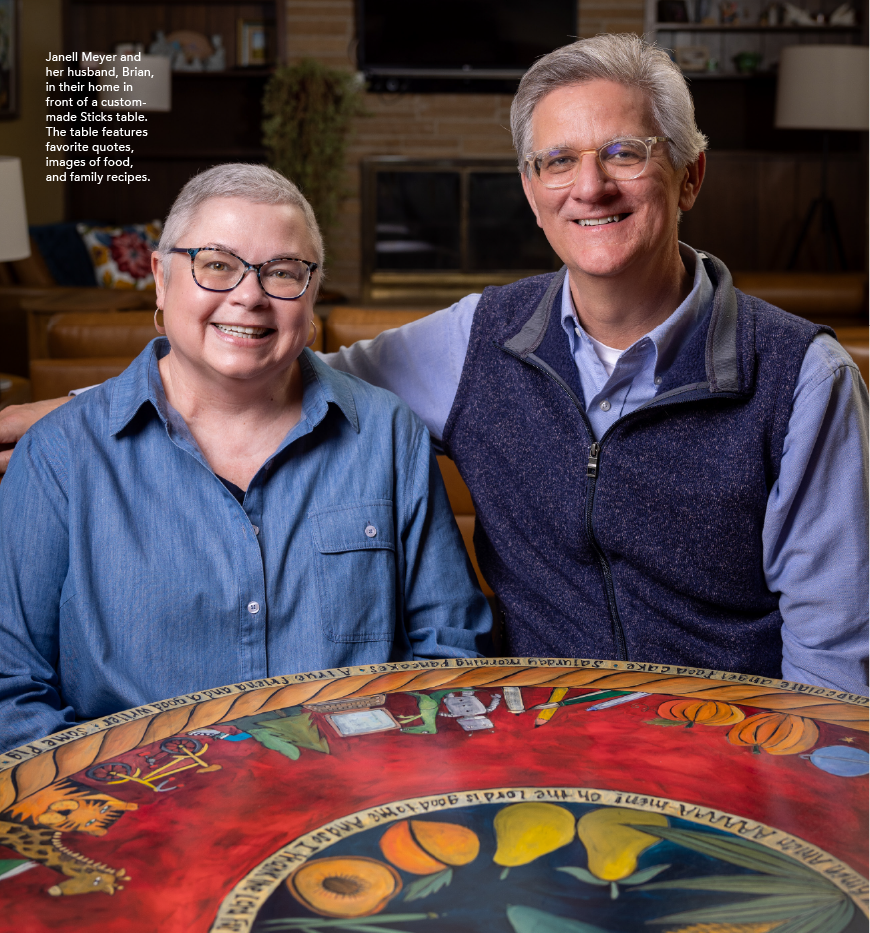 Janell Meyer and her husband, Brian, in their home in front of a custom-made Sticks table. The table features favorite quotes, images of food, and family recipes.